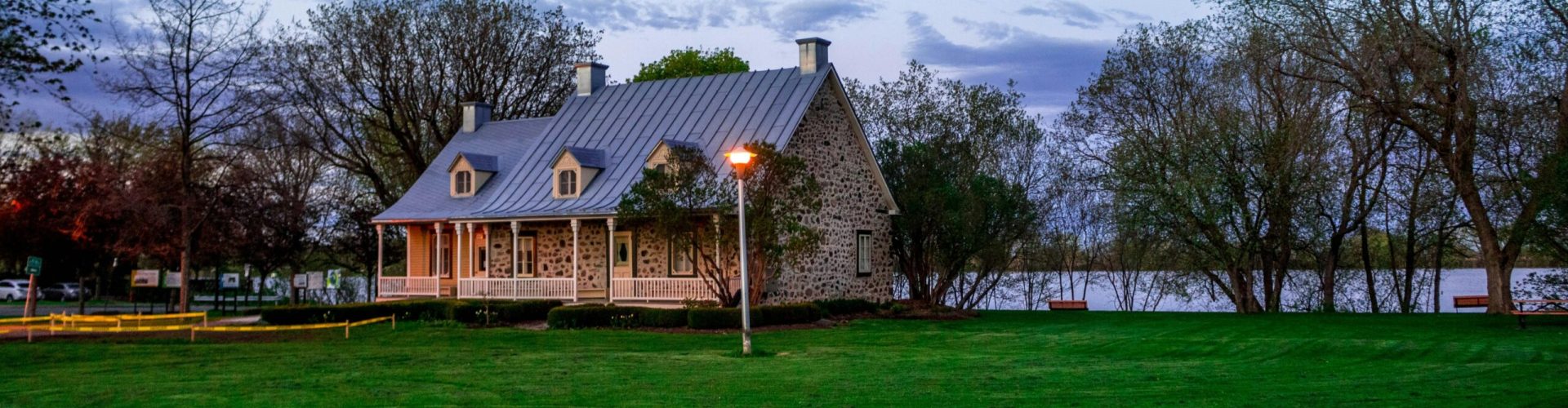Serene stone house by a lakeside with lush green lawn, ideal for real estate and architectural themes.